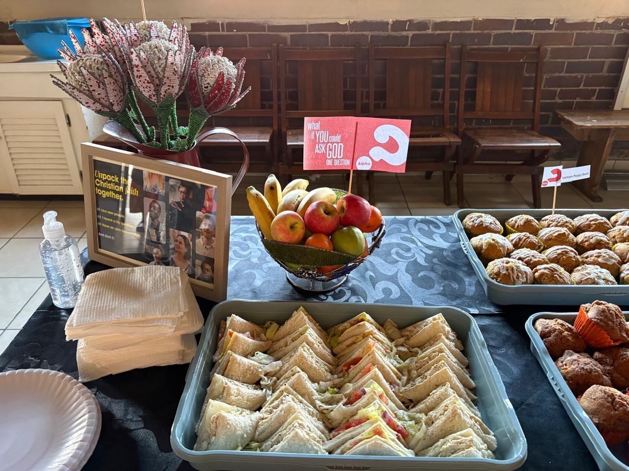 The welcome table with sandwiches, fruit and Alpha table cards